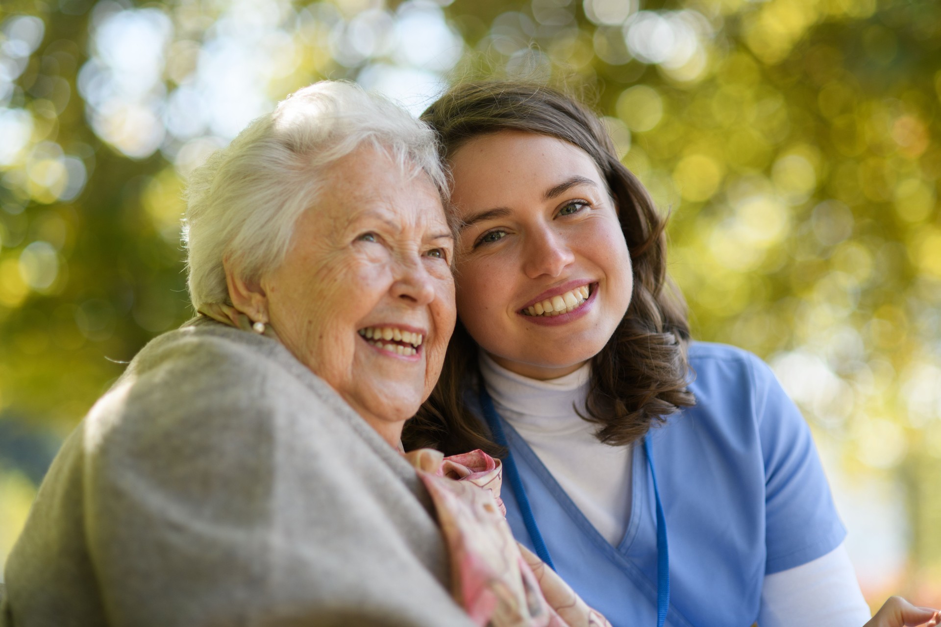 Portrait of nurse and elderly woman on walk in the park during warm autumn day. Young caregiver spending time with senior patient.