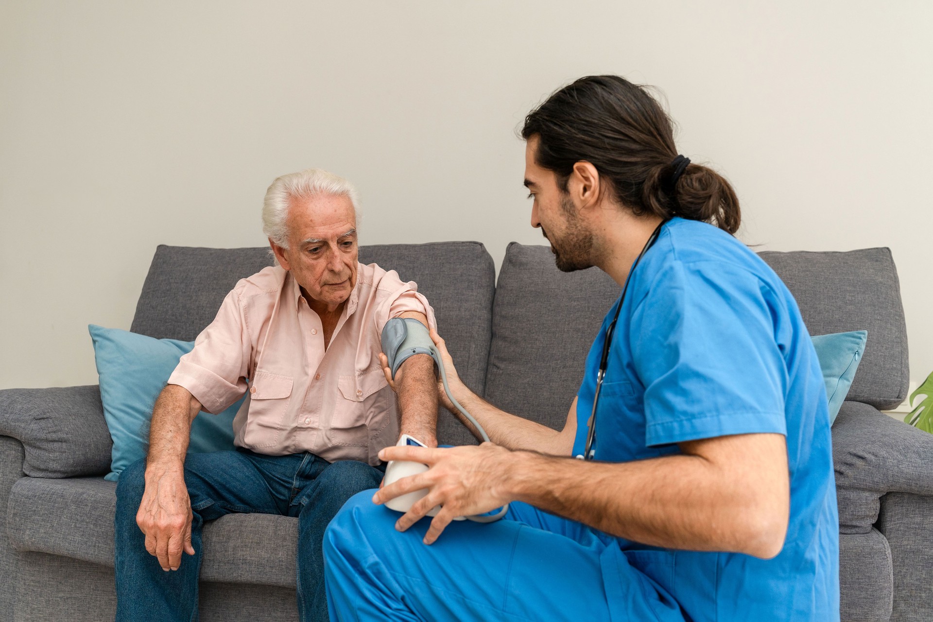 Male Nurse checking blood pressure of elderly man sitting on sofa at home